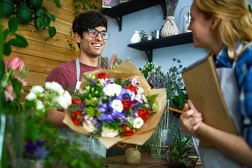 Happy florist with bouquet talking to his colleague in flower-shop