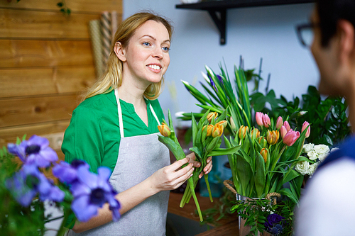 Young woman helping guy to choose tulips for his girlfriend in flower-shop