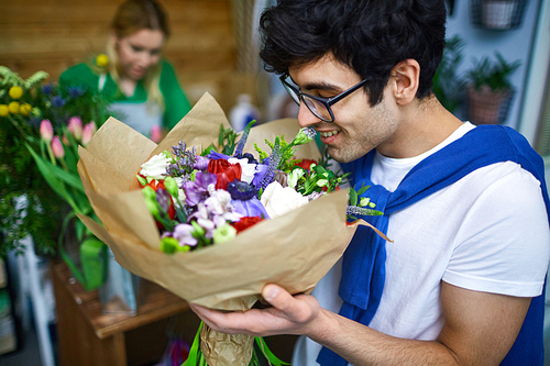 Happy young man smelling multi-floral bouquet in flower-shop