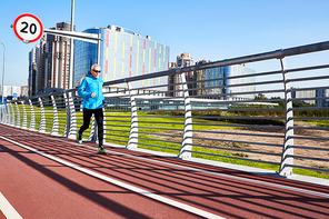 Active retired man in sportswear running down racetrack on stadium