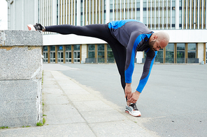 Sporty guy in activewear bending while making stretch exercise