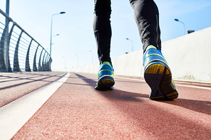 Close-up shot of sporty male legs, modern athletic track illuminated with daylight, cloudless blue sky