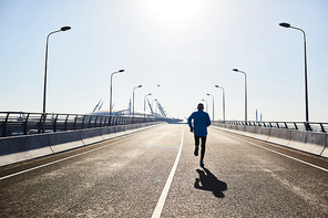 Modern road bridge illuminated with daylight, back view of senior sportsman jogging outdoors while preparing for marathon