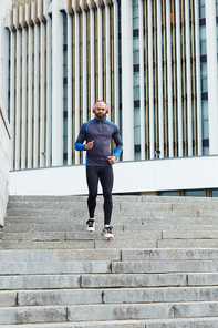 Sportsman with headphones running down staircase in the city