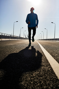 Full length portrait of confident senior man running towards camera while going in for sports outdoors, lens flare