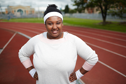 Portrait of confident overweight African woman smiling at camera before exercising at stadium