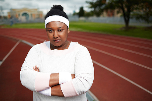 Serious African-american fat girl in activewear crossing her arms on chest while standing on stadium