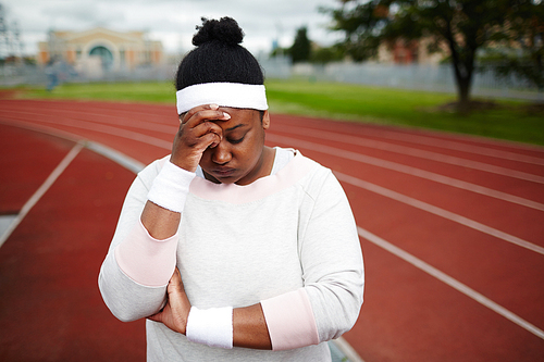 Tired chubby woman in activewear touching her forehead after training