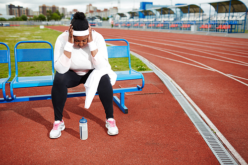 Exhausted overweight African woman recovering after tough workout at track and field stadium