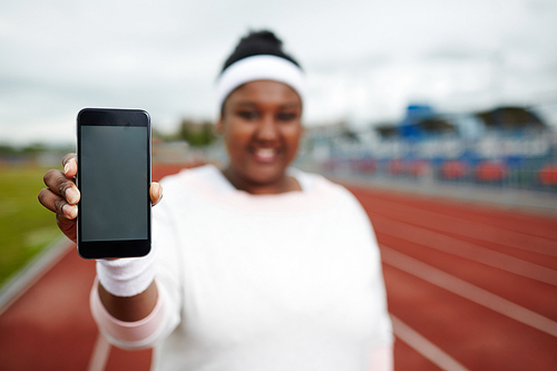 Defocused African plump woman showing screen of her smartphone while exercising at track and field stadium