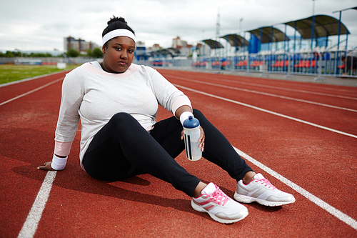 Plus-size woman in sportswear sitting on racetrack