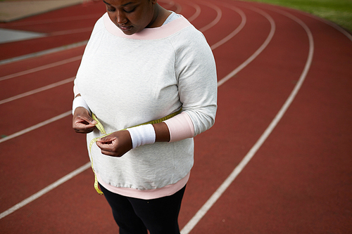 Chubby woman in sportswear measuring her waist after hard training on stadium