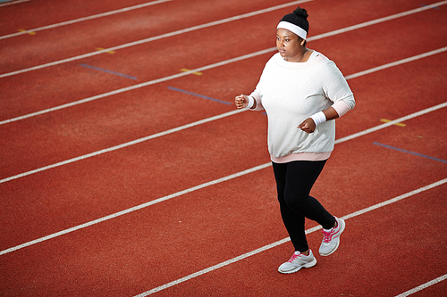 Determined overweight African woman jogging on running track to lose weight