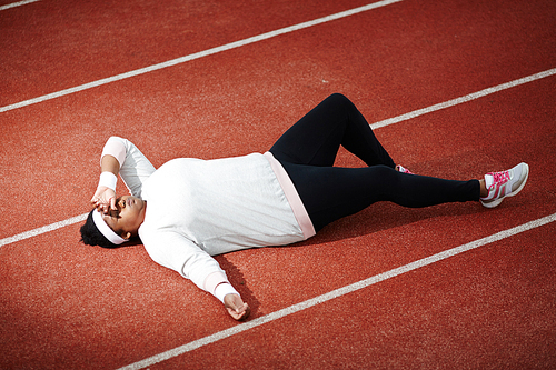 Exhausted over-sized young woman in activewear lying on racetrack after hard training