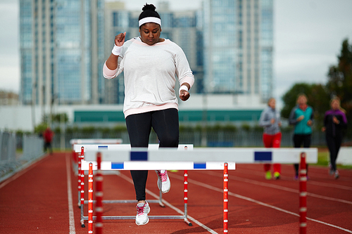 Overweight female running over hurdles on stadium