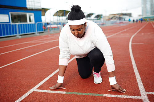 Young overweight woman standing by start line on racetrack ready to run