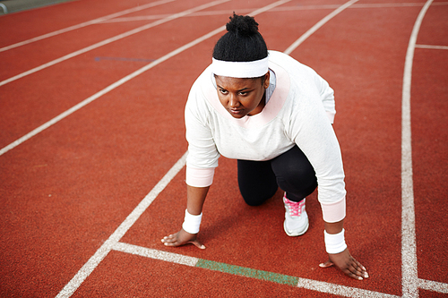 Concentrated overweight African woman preparing for run on starting line