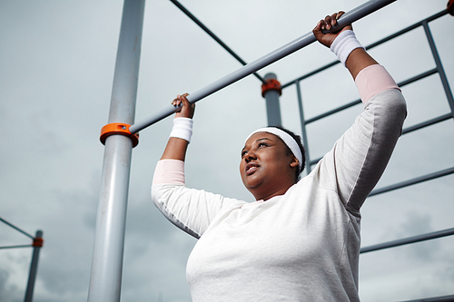 Determined overweight African woman practicing pull-up exercise outdoors