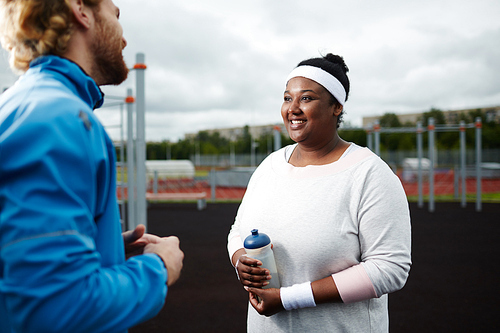 Happy young over-sized woman talking to her trainer at sports ground