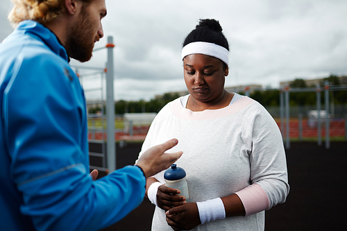 Weight-loss coach motivating frustrated plus-size African woman at outdoor workout area