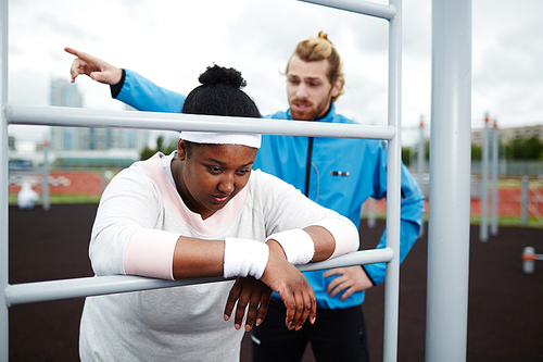 Young trainer making plus-sized woman work harder and motivating her to continue exercising