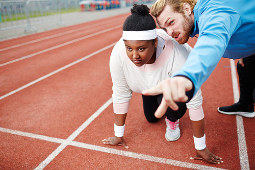 Sport trainer pointing out goal for young overweight female at low start before running