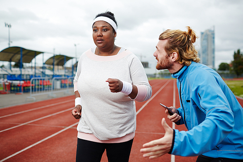Professional trainer encouraging young chubby woman to run faster before finish
