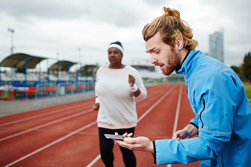 Personal trainer measuring time on smartphone while overweight female client running on track