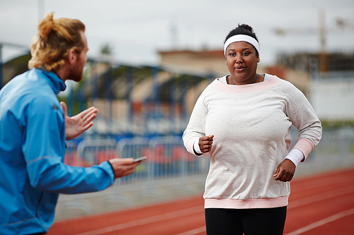 Fat young woman in activewear approaching finish line while trainer giving her recommendations about keeping breath