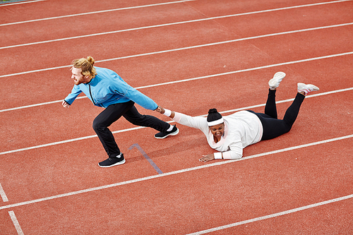 Determined personal trainer dragging exhausted overweight woman on track motivating her to keep running