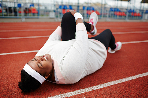 Young overweight woman lying on race track and doing exercise for legs