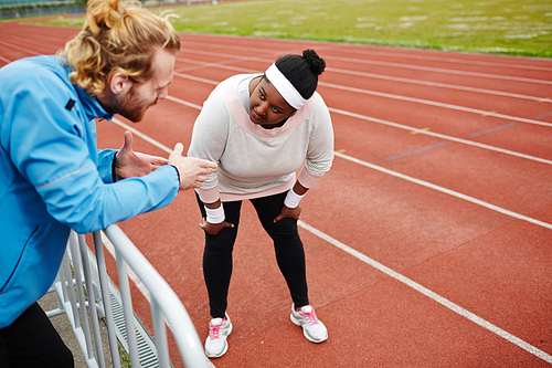 Young sporty plus-size girl listening to her trainer advice during workout on stadium
