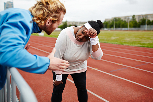 Tired plus-size woman being motivated by personal trainer on running track
