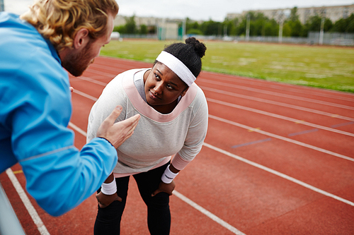 Oversized woman listening to her trainer consultation during workout at stadium