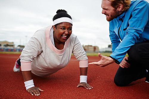 Determined plus-size woman doing push ups motivated by personal coach