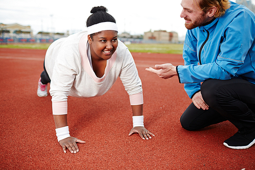 Young trainer encouraging oversized female during workout on stadium