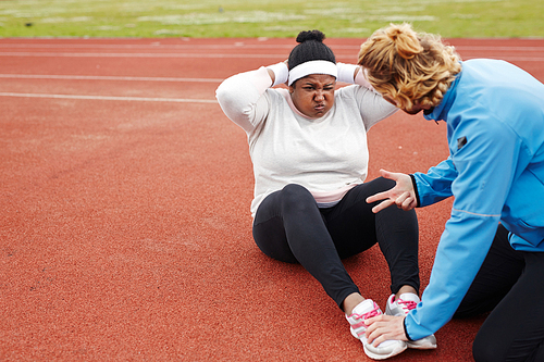 Plus-size African woman doing sit-ups exercise guided by personal trainer