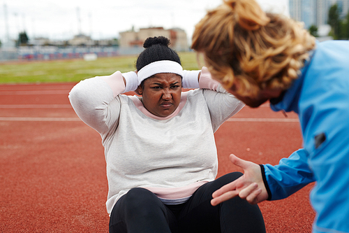 Determined plus-sized woman doing difficult exercise with her trainer help