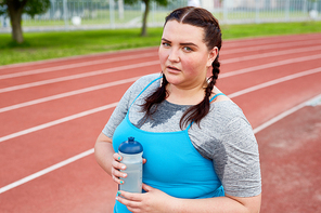 Sweating obese woman with bottle of water having short rest between workout sets