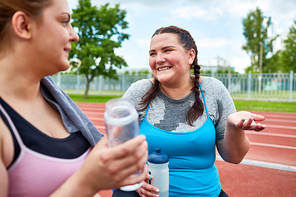 Young women with water having talk and refreshment at stadium after running