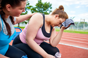 Stressed young plump female with towel and bottle of water expressing tiredness while friend comforting her