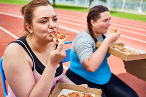 Hungry over-sized females eating pizza after workout on stadium