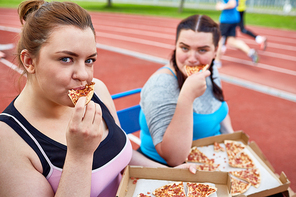 Hungry obese women eating delicious takeout pizza after physical training