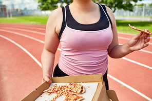 Chubby female in black and pink tanktops eating pizza slice by slice during training on stadium