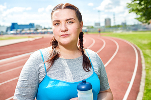 Young plump woman with pigtails standing on stadium and having break after workout