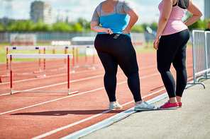 Two plump friends in sportswear standing on racetrack of stadium