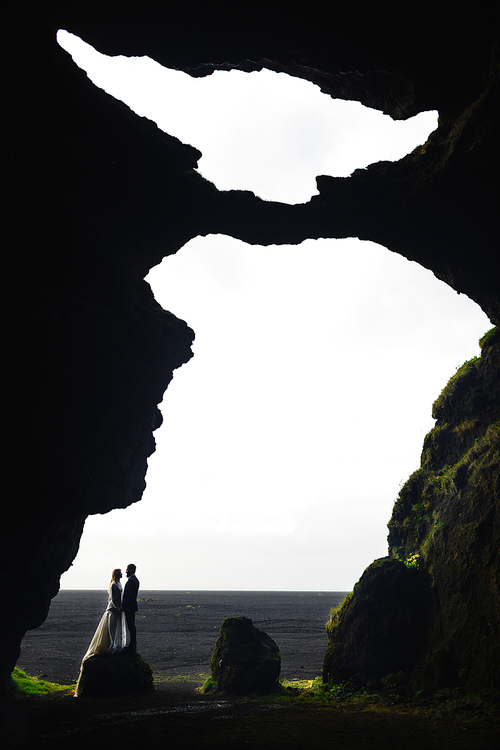 Newlyweds standing on stone by cave entrance