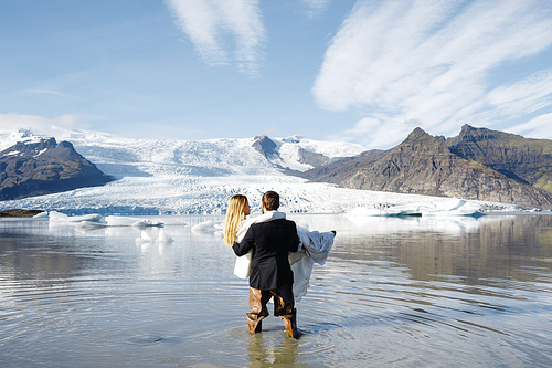 Young man standing in water with his wife on hands and both enjoying majestic scenery