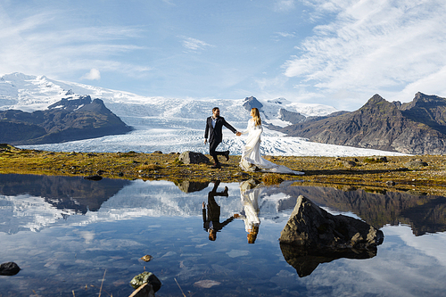 Newlyweds running along coastline of northern lake