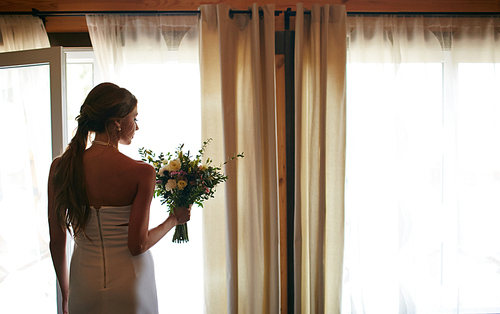 Back of bride with bouquet standing by window